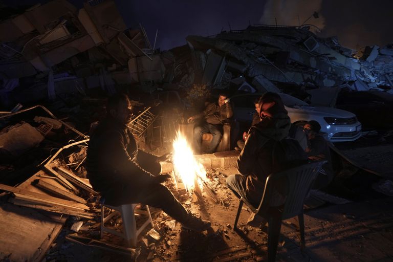 Pessoas se aquecem ao redor de uma fogueira em frente a prédios destruídos por um forte terremoto, em Antakya, sul da Turquia, em 8 de fevereiro de 2023. (AP Photo/Khalil Hamra)